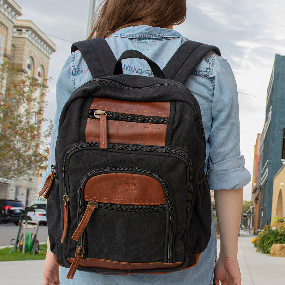 Woman wearing a Retro Londoner Commuter Daypack walking through a small downtown area during a cloudy day. 