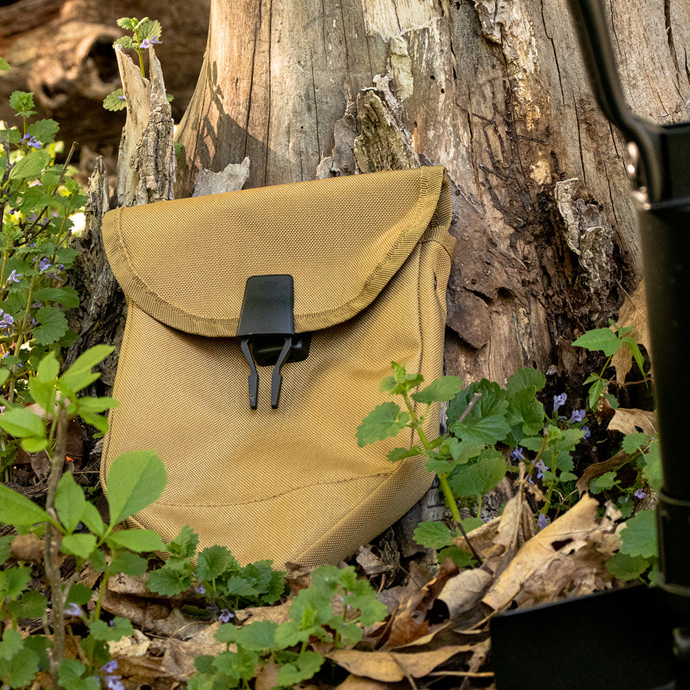 GI Style Tri-fold Shovel Cover in front of a old tree trunk surrounded by small purple wildflowers.