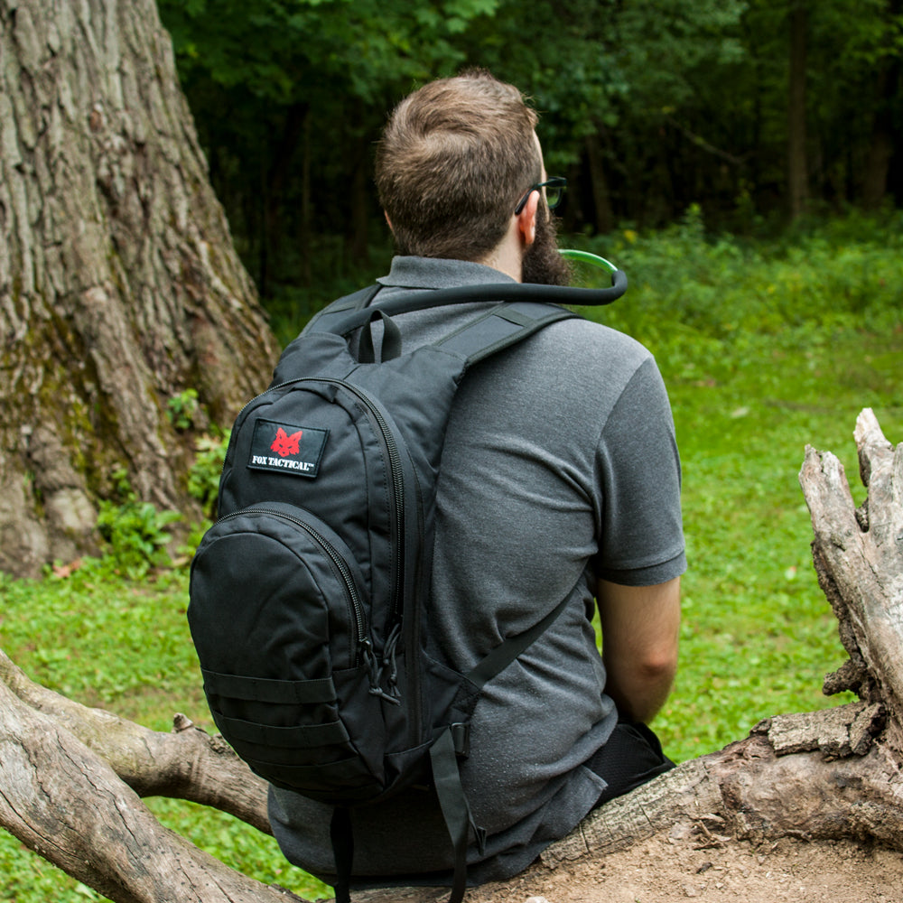 Man sitting on a log drinking from the Compact Modular Hydration Pack's hose. 