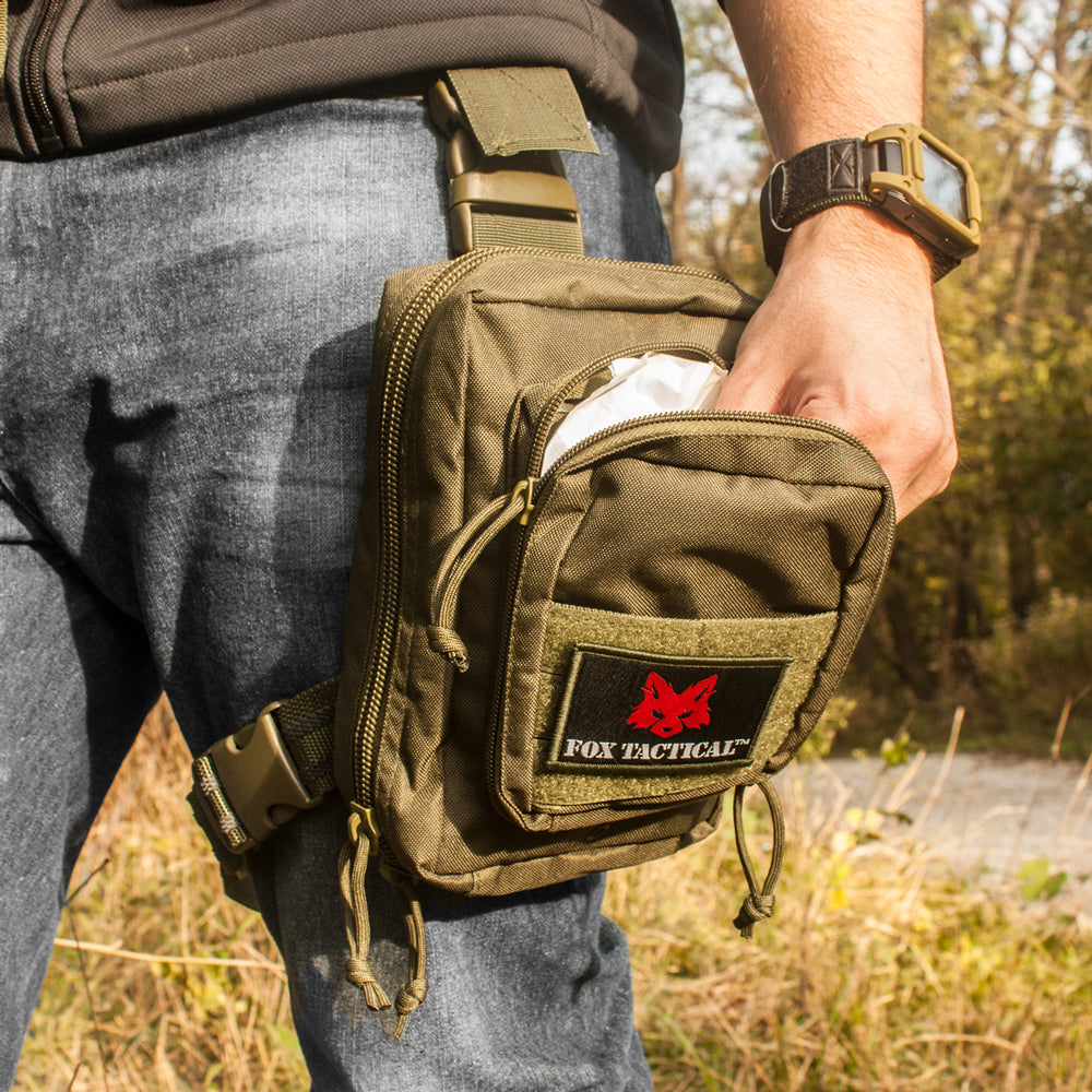 Man standing in a field reaching into the Drop Leg First Responder System Pouch on his leg. 