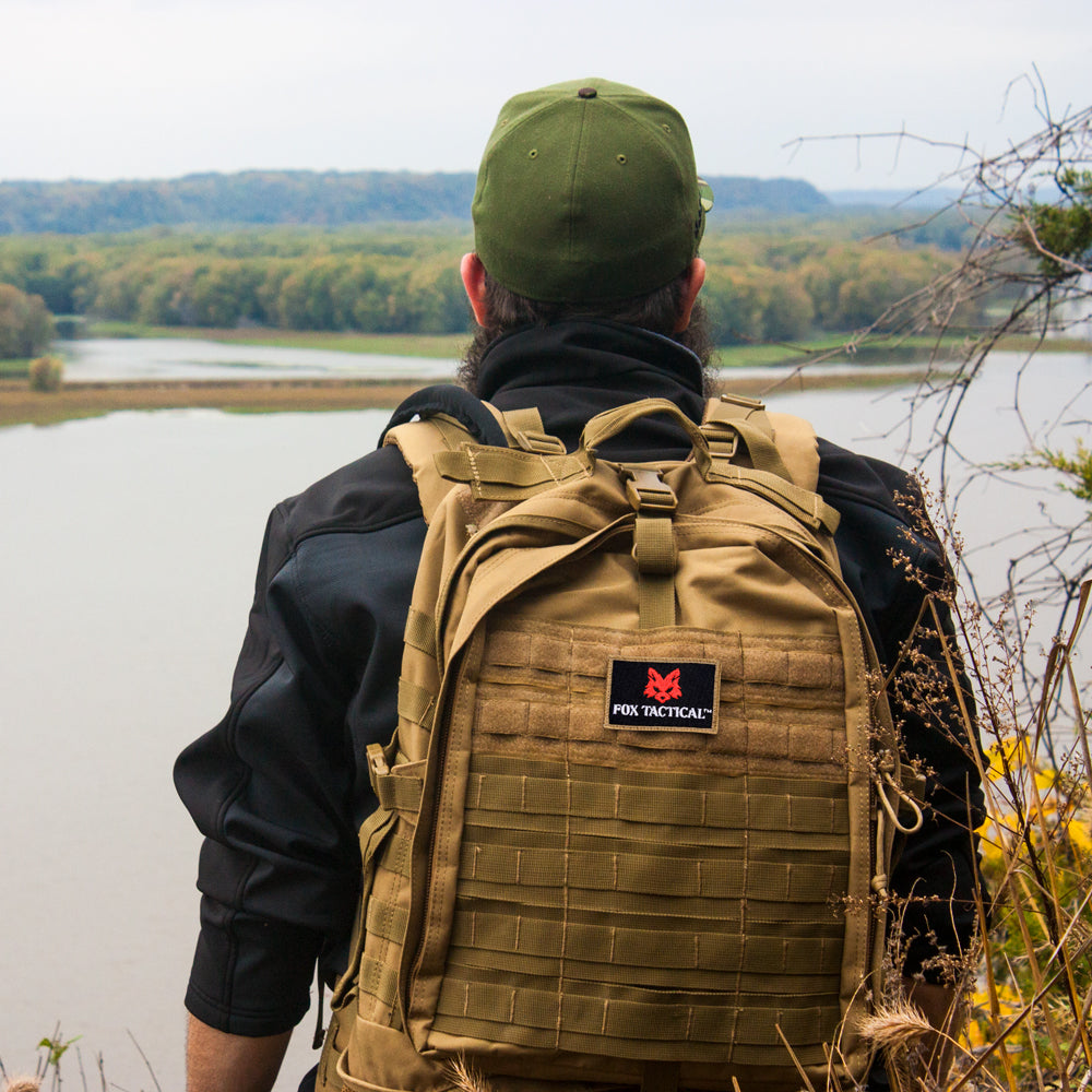Man on a cliff looking across a wide river wearing a Stealth Reconnaissance Pack. 