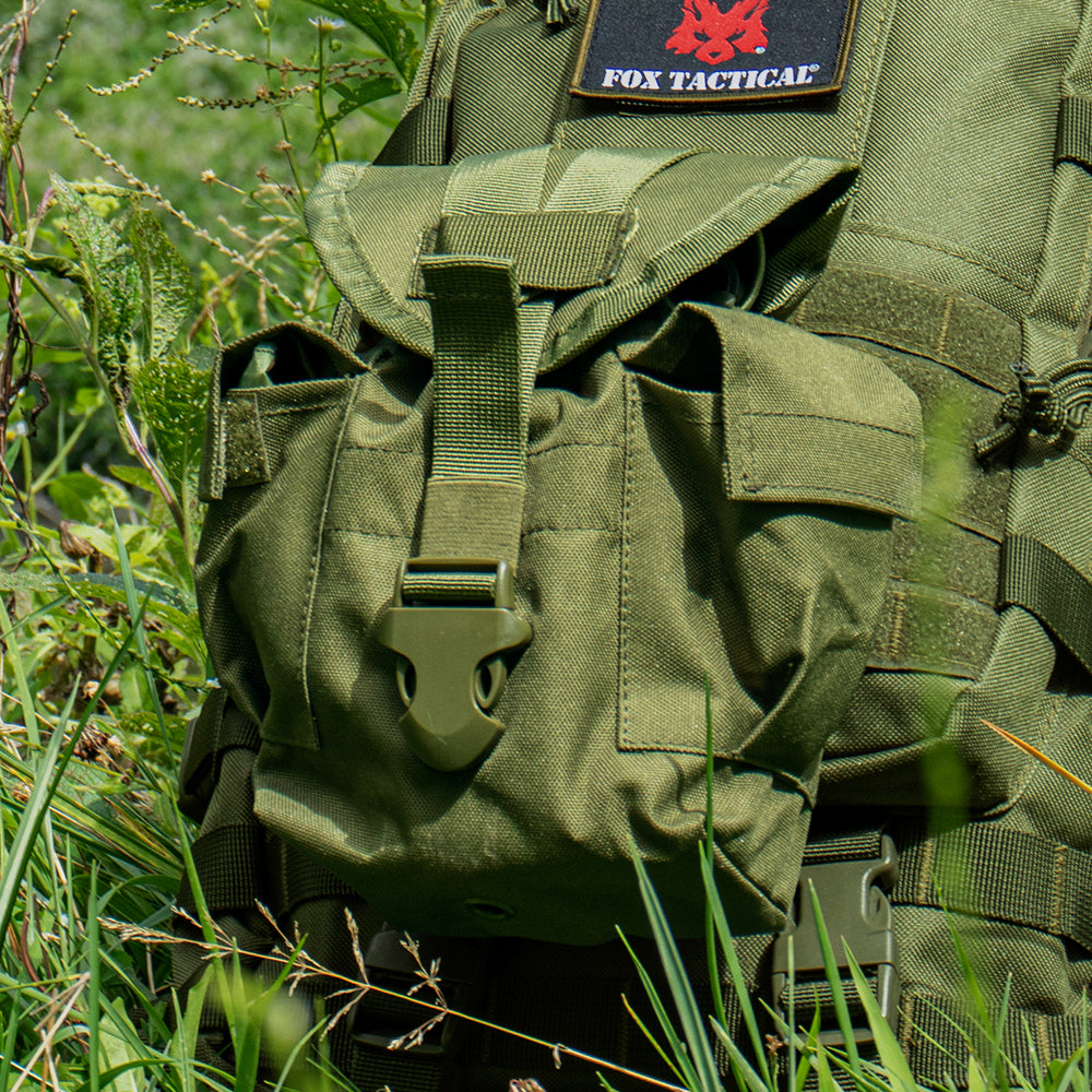 Modular 1 Quart Canteen Cover attached via modular web straps to a tactical bag laying in a sunny, grassy field. 