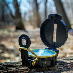Plastic Lensatic Compass sitting in the sun on a log in the woods.