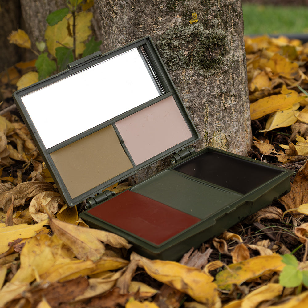 Camouflage Compact Face Paint open and laying on yellow fallen leaves in front of a small tree. 