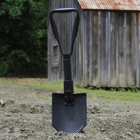 GI Spec Trifold Shovel stuck in the dirt in front of an old barn shed.