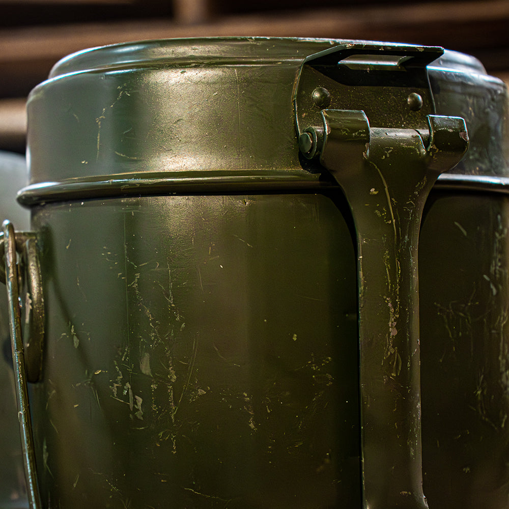 Closeup of a Romanian 2-Piece Aluminum Mess Kit in a dark room with a bright light shining on it.