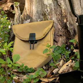 GI Style Tri-fold Shovel Cover in front of a old tree trunk surrounded by small purple wildflowers.
