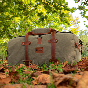 Weekender Duffel Bag on top of fallen leaves in a sunny, grassy field.