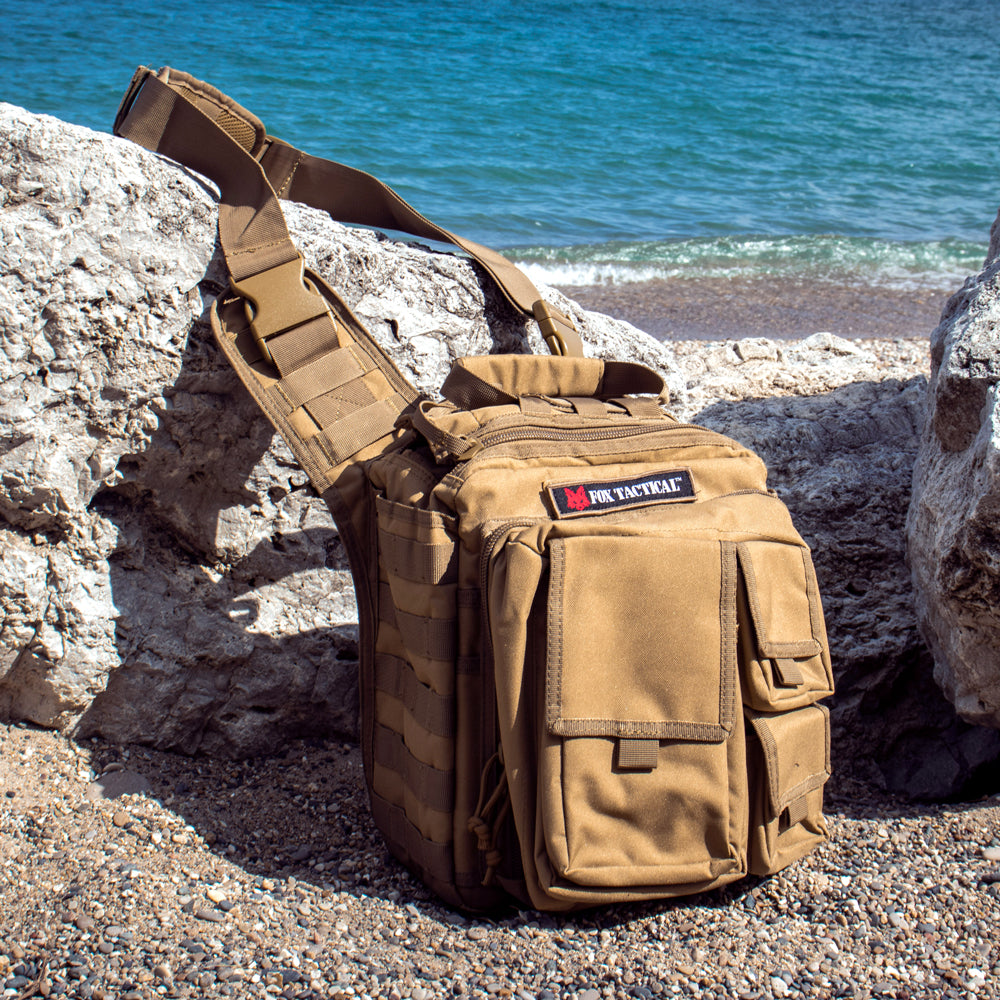 Over The Headrest Tactical Go-To Bag laying against a rock on the beach with small waves behind.