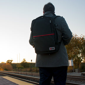 Man waiting at a train stations wearing a Voyager Hybrid Travel Pack. 54-541